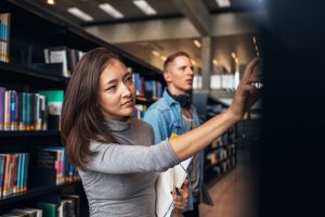 University students taking book from shelf in library